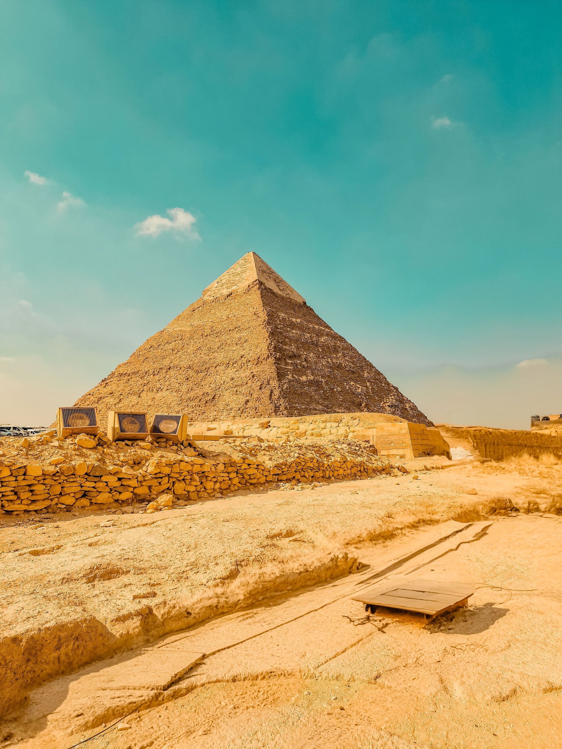 Een piramide in een zanderige woestijn onder een helderblauwe hemel, met een zandpad op de voorgrond.