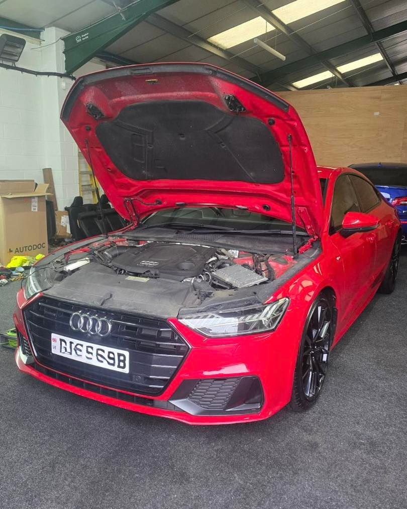 Red Audi A7 with its hood open in a garage, revealing the engine. Black wheels.