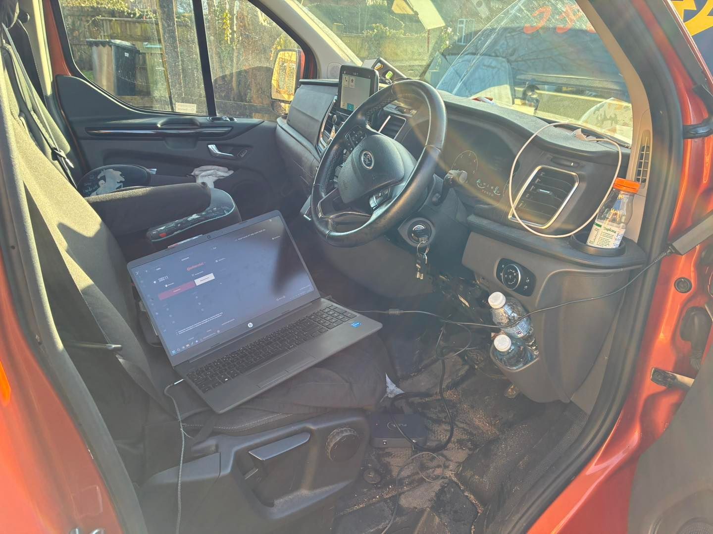 Interior of a damaged orange van with a laptop on the passenger seat, windshield cracked.
