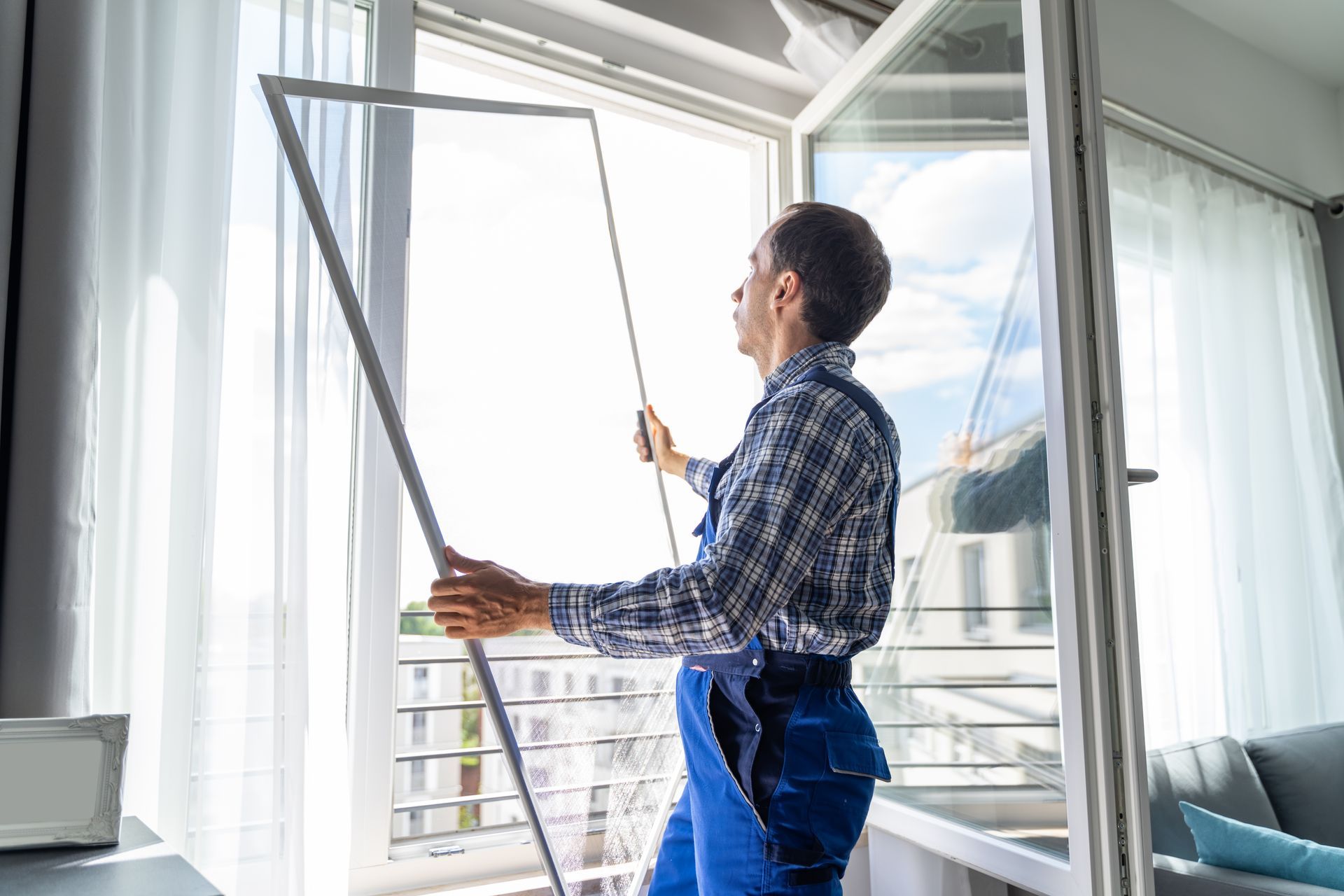 Person installing a window screen in a bright apartment with city view