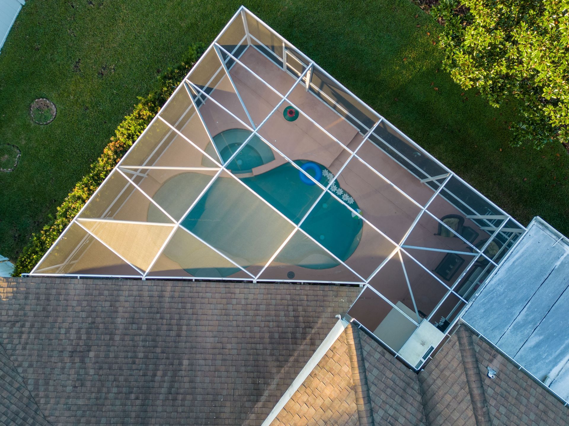 Aerial view of a screened backyard pool beside a house and lawn