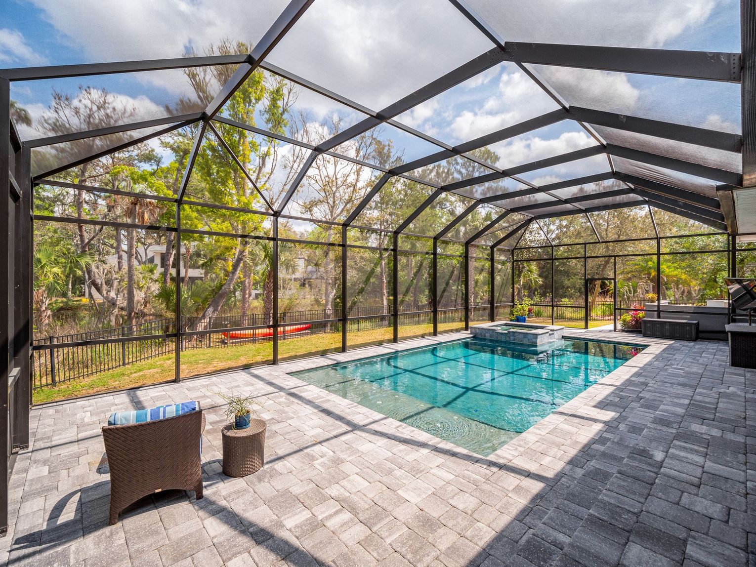 Screened-in patio with a pool, paver deck, and outdoor seating under a sunny sky