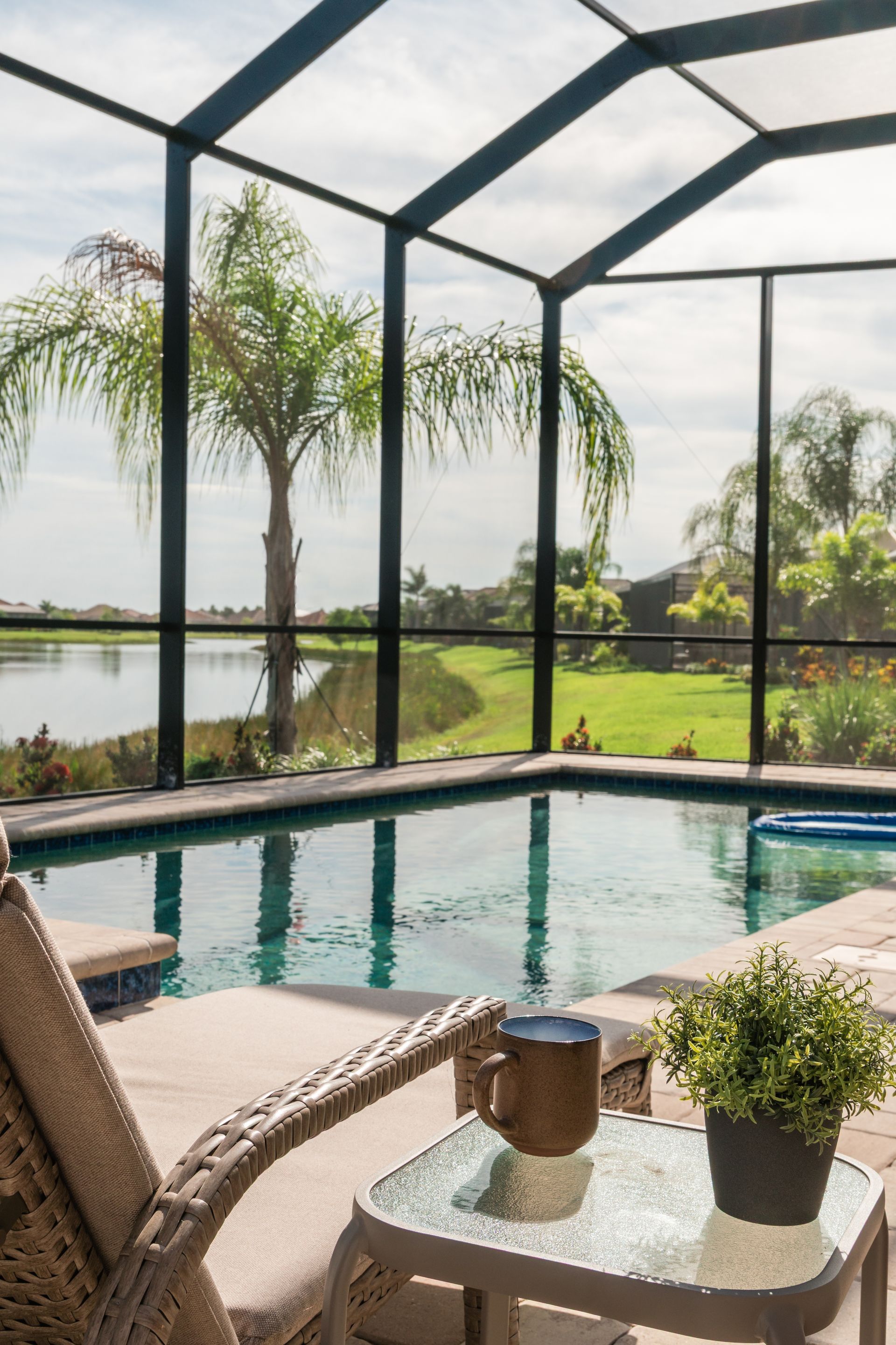 Screened patio with a swimming pool, patio chairs, and a lake view beyond palm trees.