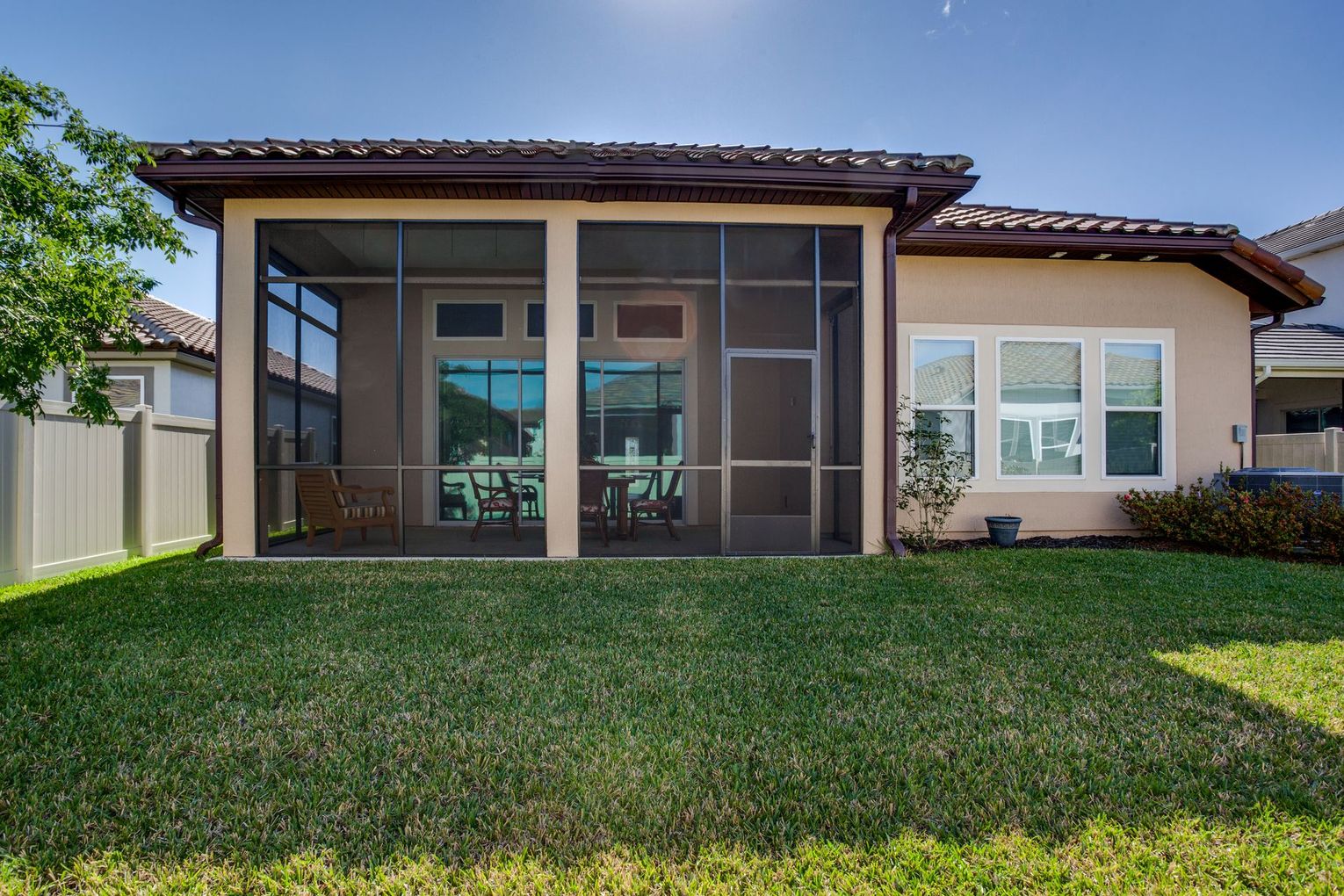 Backyard view of a house with screened patio, green lawn, and white fence