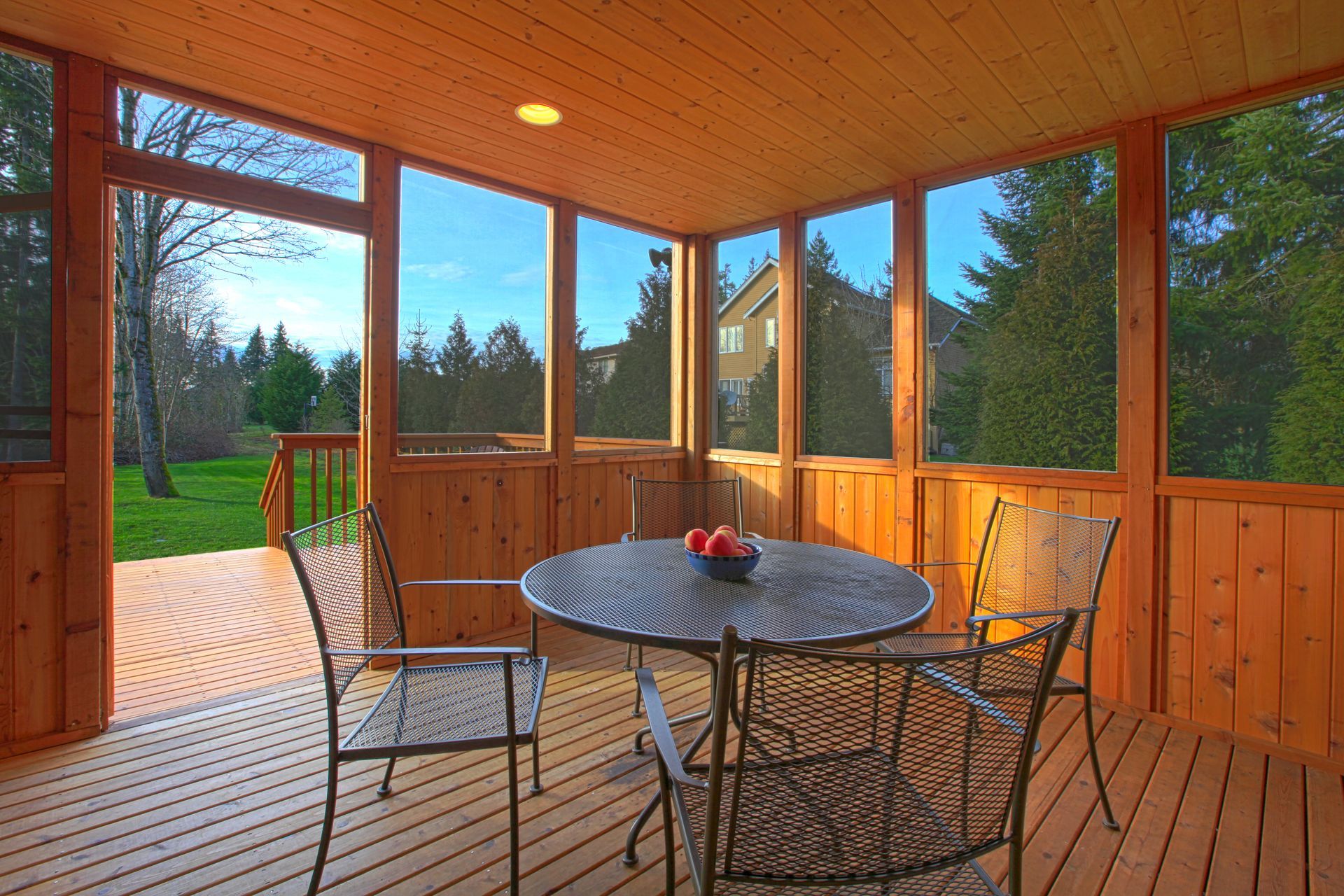 Screened porch with wood paneling, round table, chairs, and view of green yard and trees