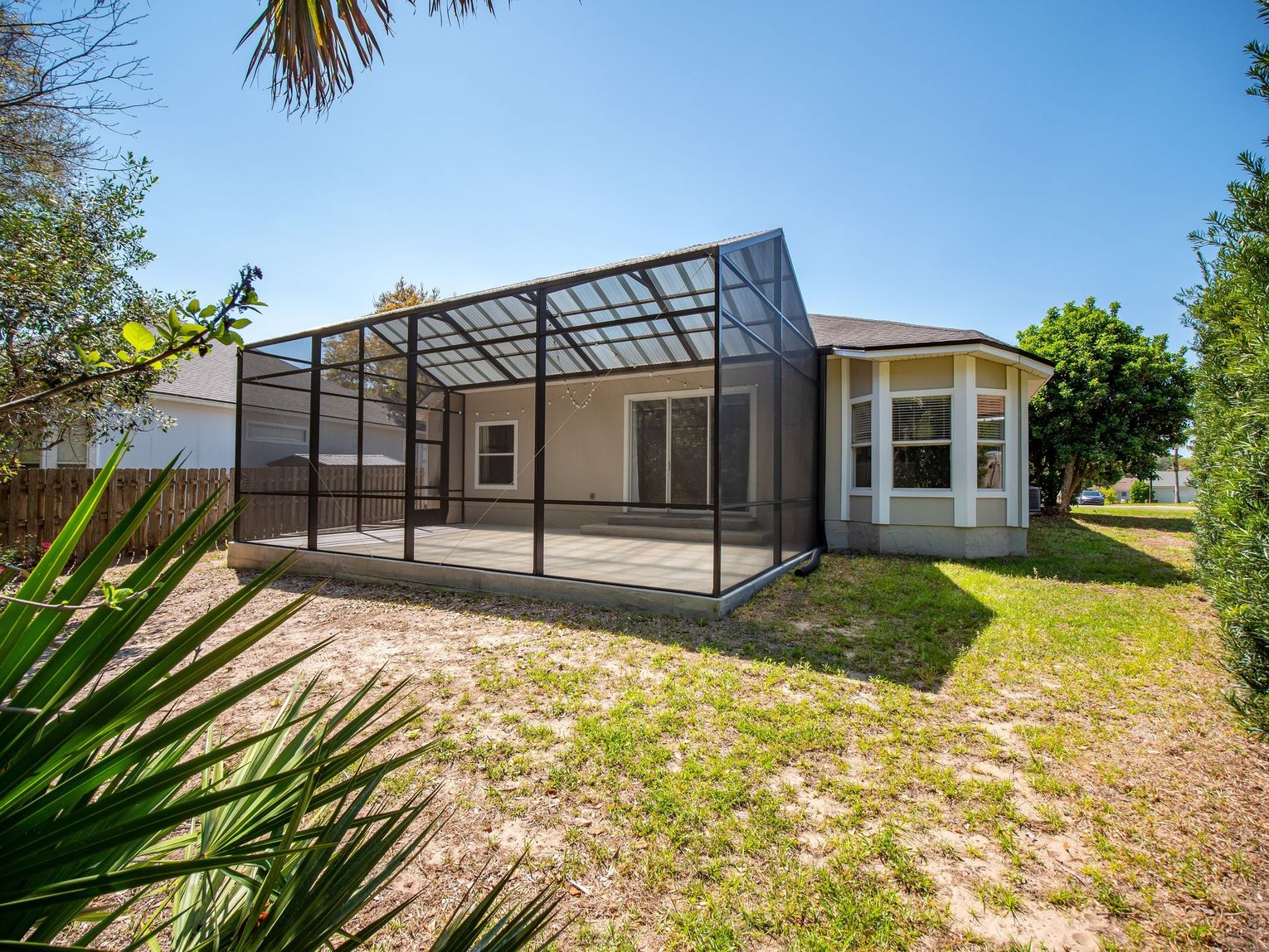 Backyard patio with screened enclosure beside a white house, grassy yard and palm trees