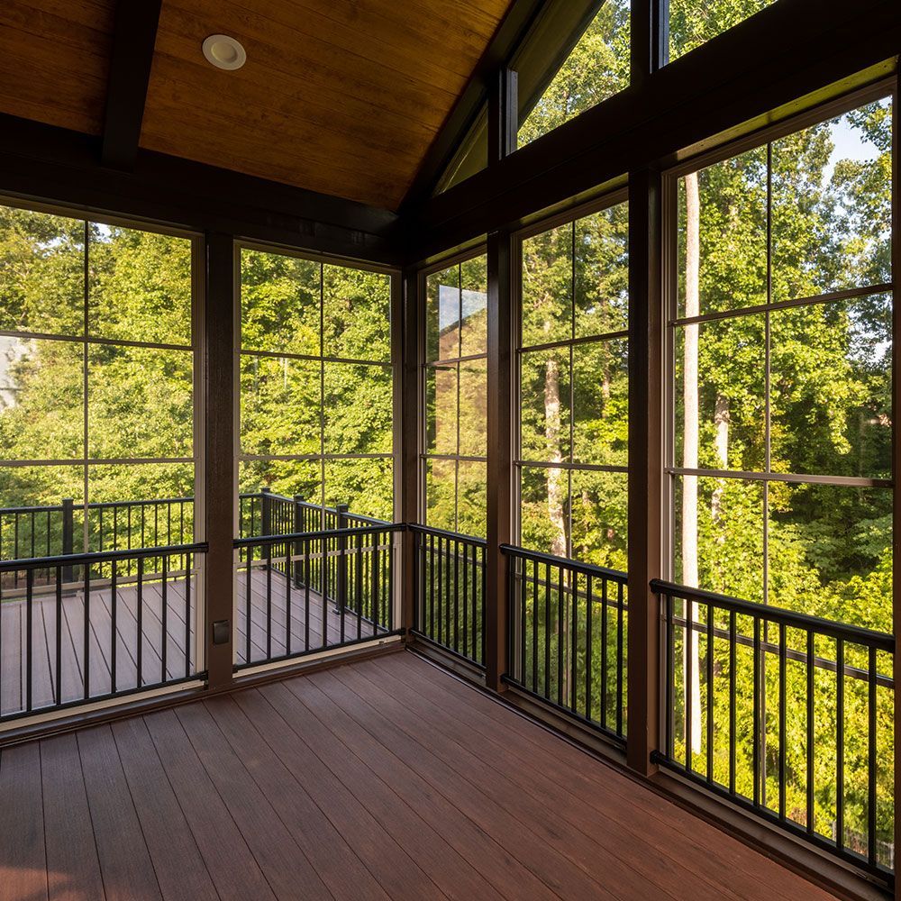 Screened porch with dark railing, wood floor, and large windows overlooking green trees