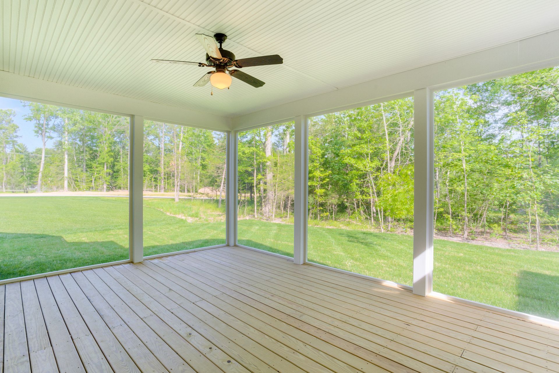 Covered screened porch with ceiling fan, white railings, and wooded yard view through open screens