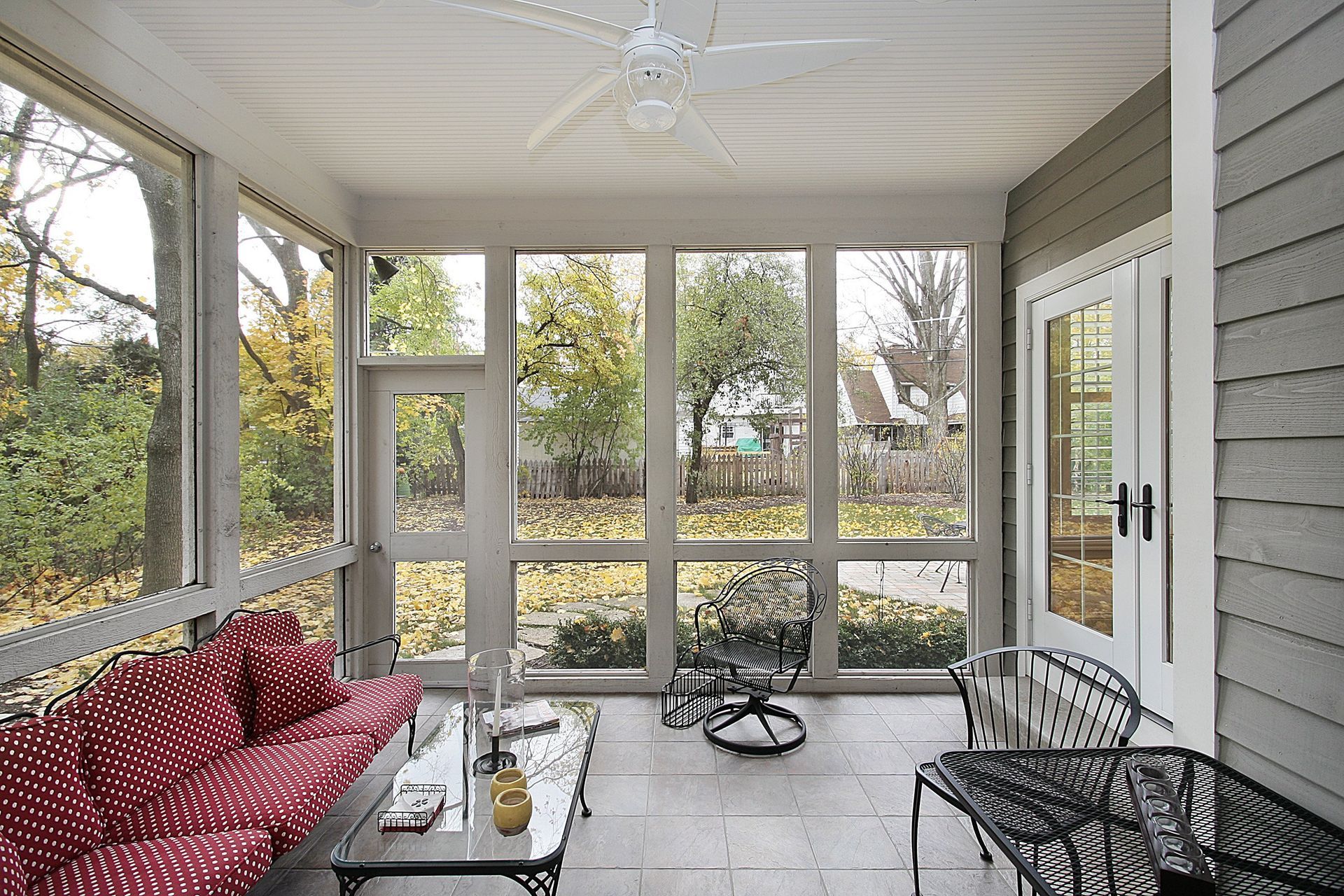 Screened porch with red bench, wicker chairs, and a small table overlooking a yard.