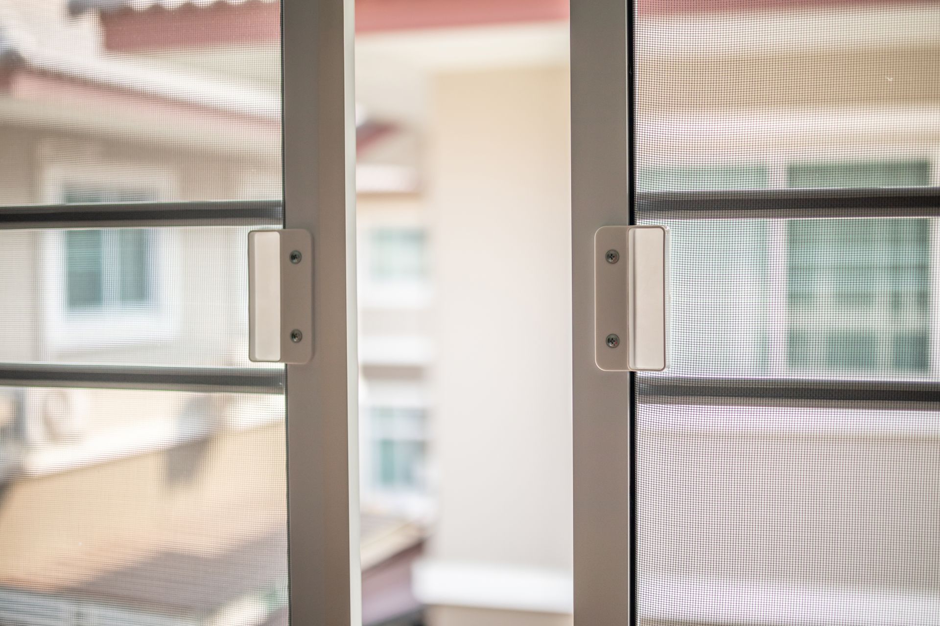Sliding screen door partly open with balcony and apartment buildings visible beyond.