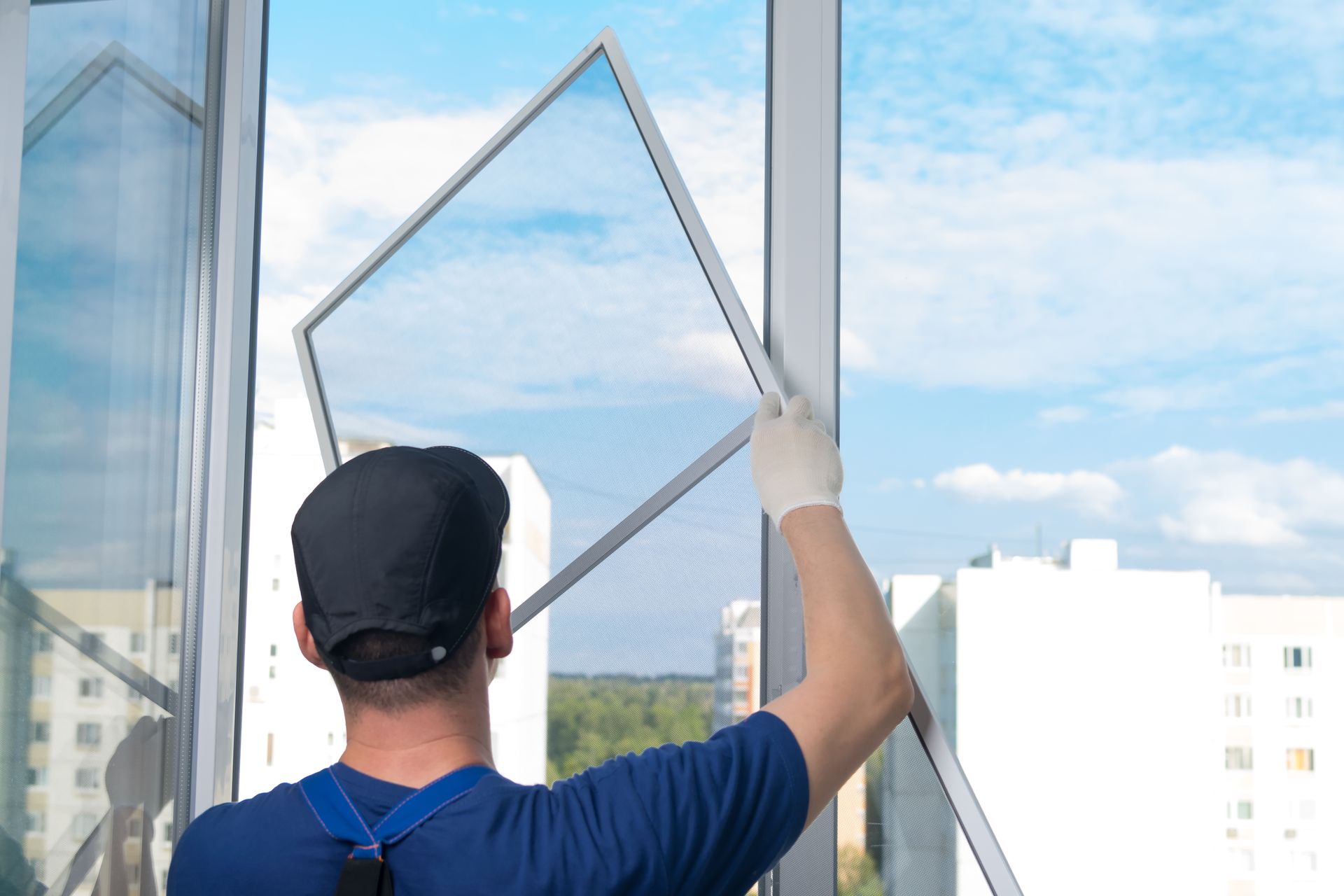 Person cleaning a window with a squeegee, viewed from behind against a bright city skyline.
