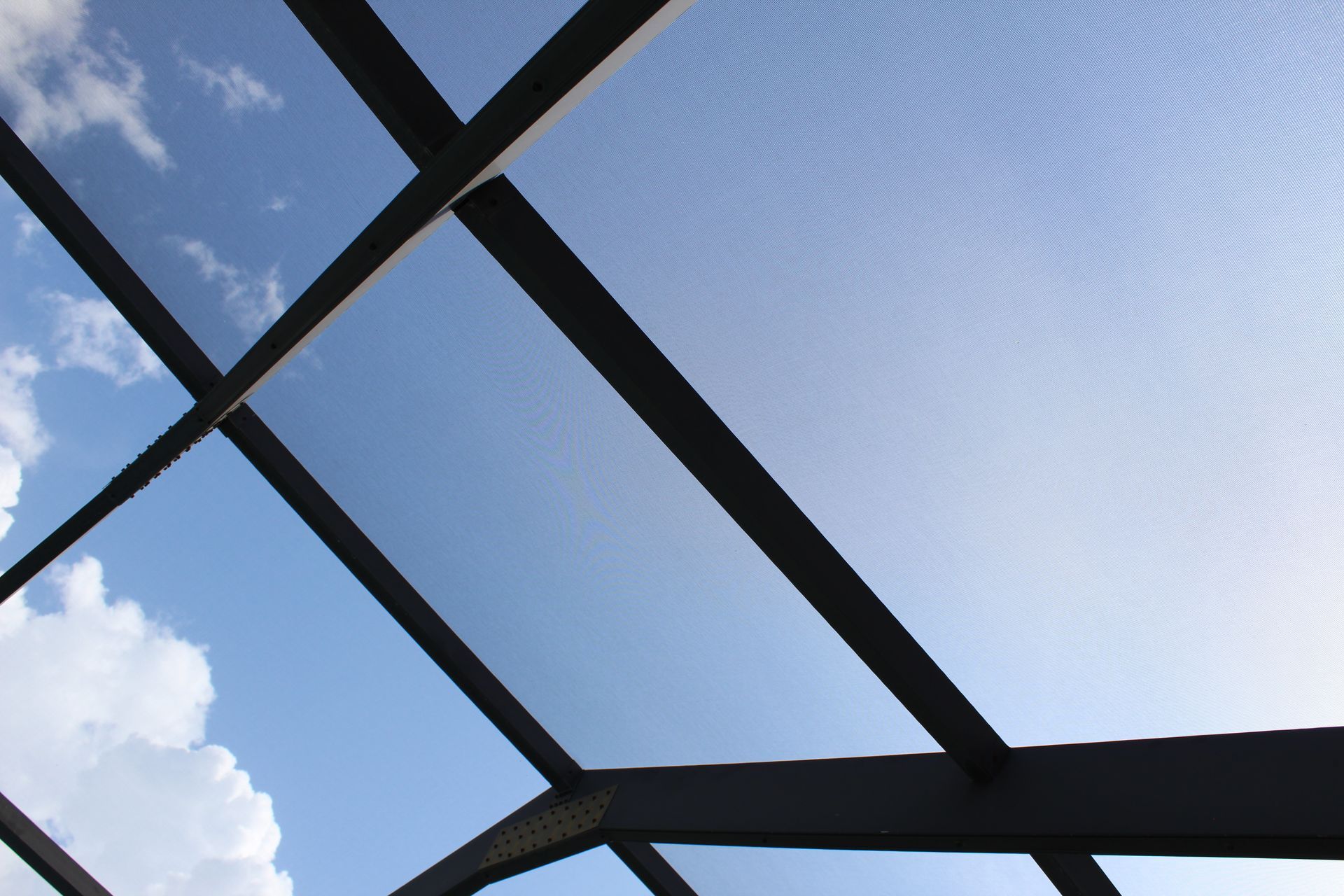 Blue sky seen through dark metal roof beams and glass panels