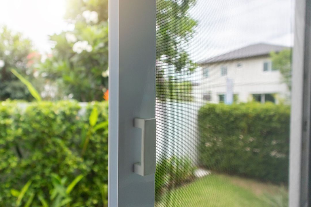 Partially open window overlooking a green yard and neighboring house