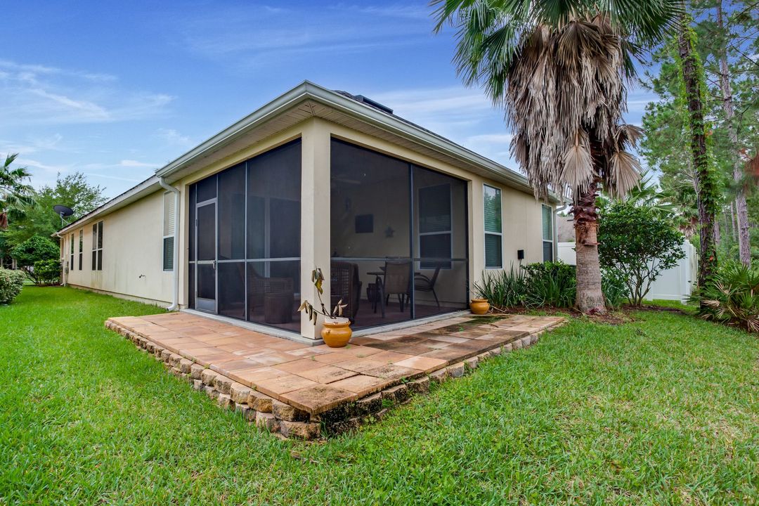 Single-story house with screened porch, tan siding, and green lawn in a tropical yard