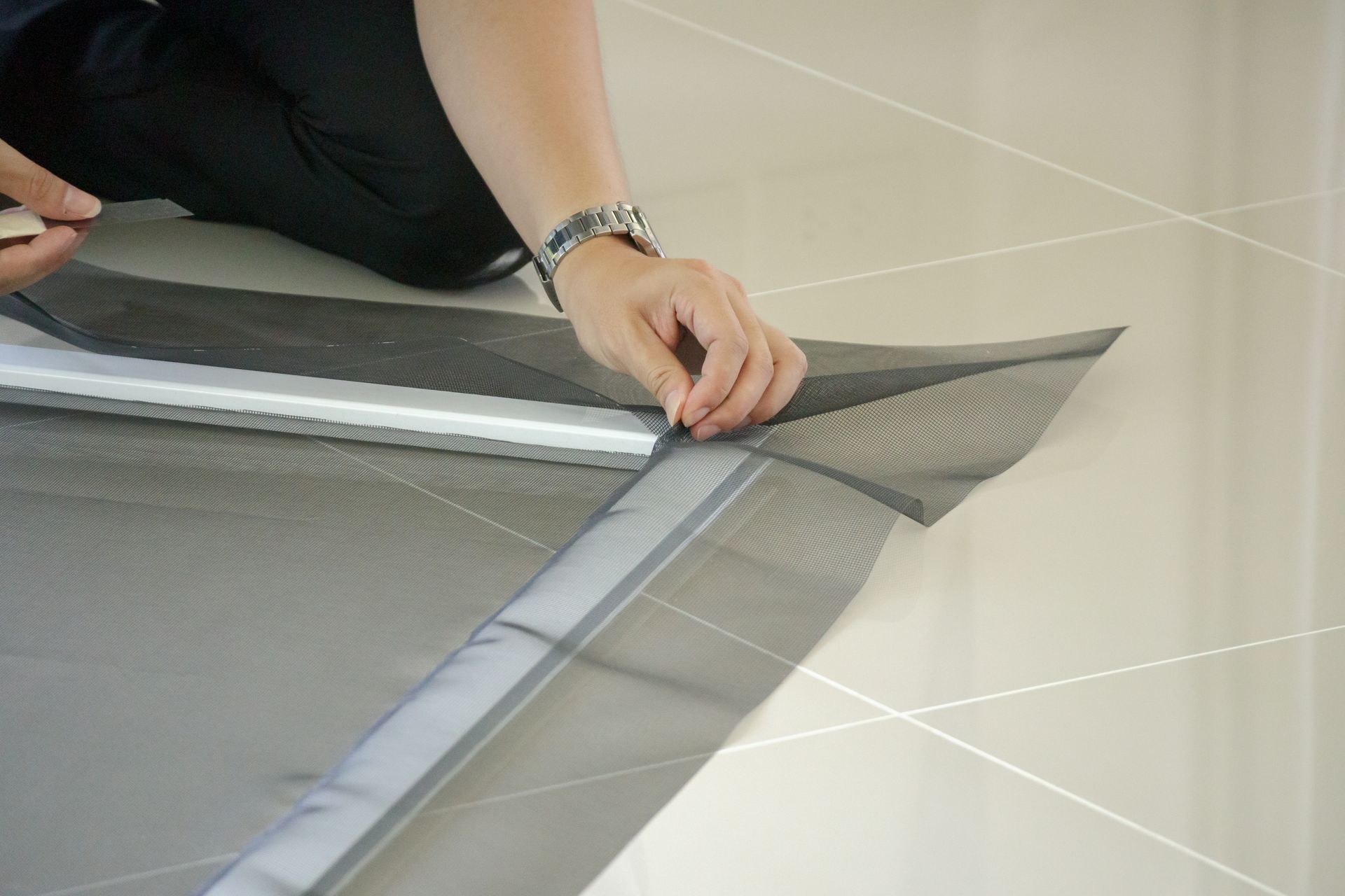 Hands folding the edge of a gray mesh screen on a tiled floor
