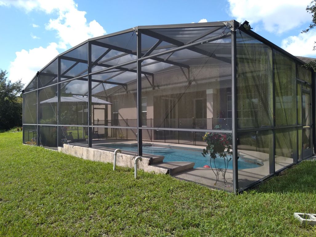 Indoor swimming pool under a screened, peaked enclosure with clear blue water and patio decking.
