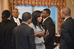 Group of elegantly dressed Black people in a room, conversing. Woman in grey suit gestures.