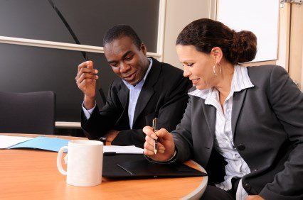 Man and woman in business attire reviewing documents at a table, discussing work.