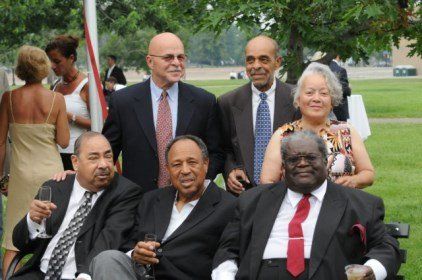 Group of formally dressed people, mostly men, posing outdoors, smiling.