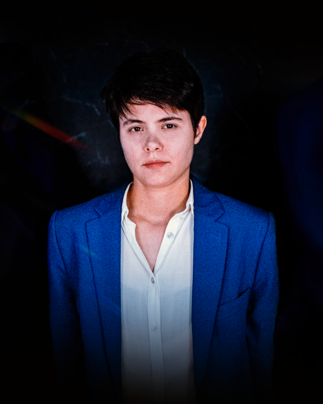 Mulher de blazer azul e camisa branca contra um fundo escuro, olhando para a frente.