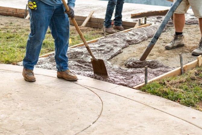 Workers pouring and smoothing concrete on a sidewalk next to a curb.