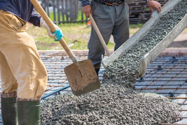 Workers pouring wet concrete onto steel rebar at a construction site
