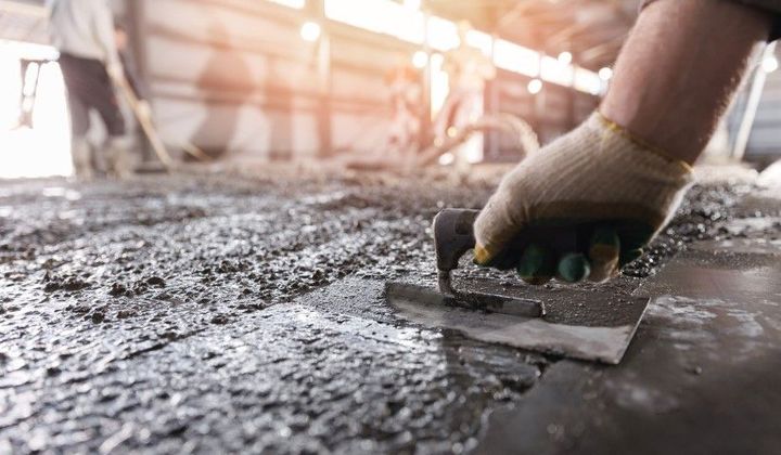 Worker smoothing wet concrete with a trowel at a construction site