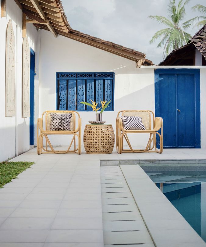 Blue-and-white patio with wicker chairs, a woven table, and a pool beside a white house