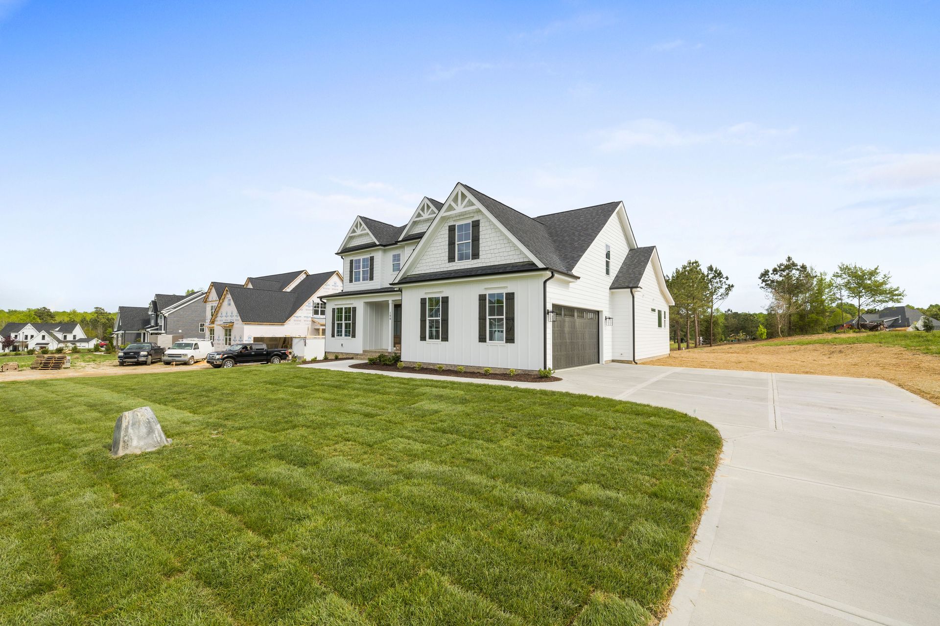 Large white suburban house with a gray roof beside a curved driveway and green lawn under a clear blue sky