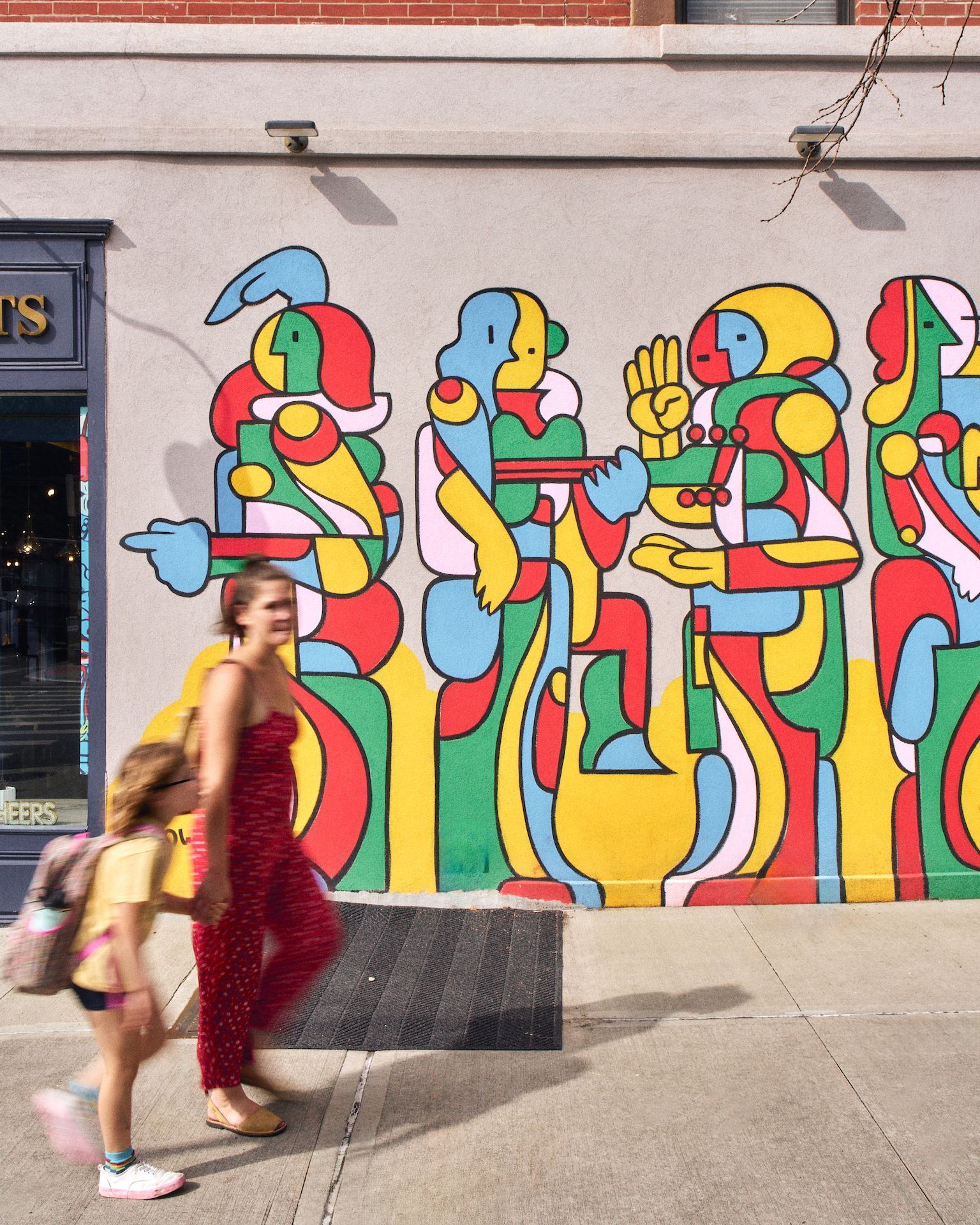 A woman and child are walking in front of a colorful mural on the side of a building