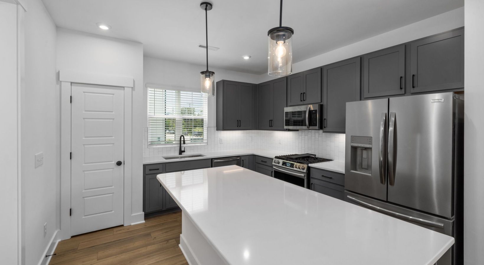 Modern kitchen with gray cabinets, white countertops, stainless steel appliances, and two hanging pendant lights.