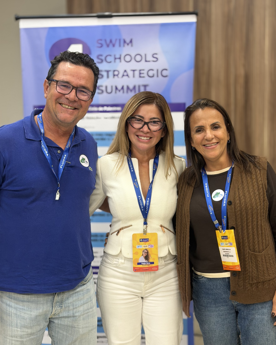 Tres asistentes sonrientes posan frente al telón de fondo de la Cumbre Estratégica de Escuelas Suizas, luciendo cordones acreditativos de la conferencia.