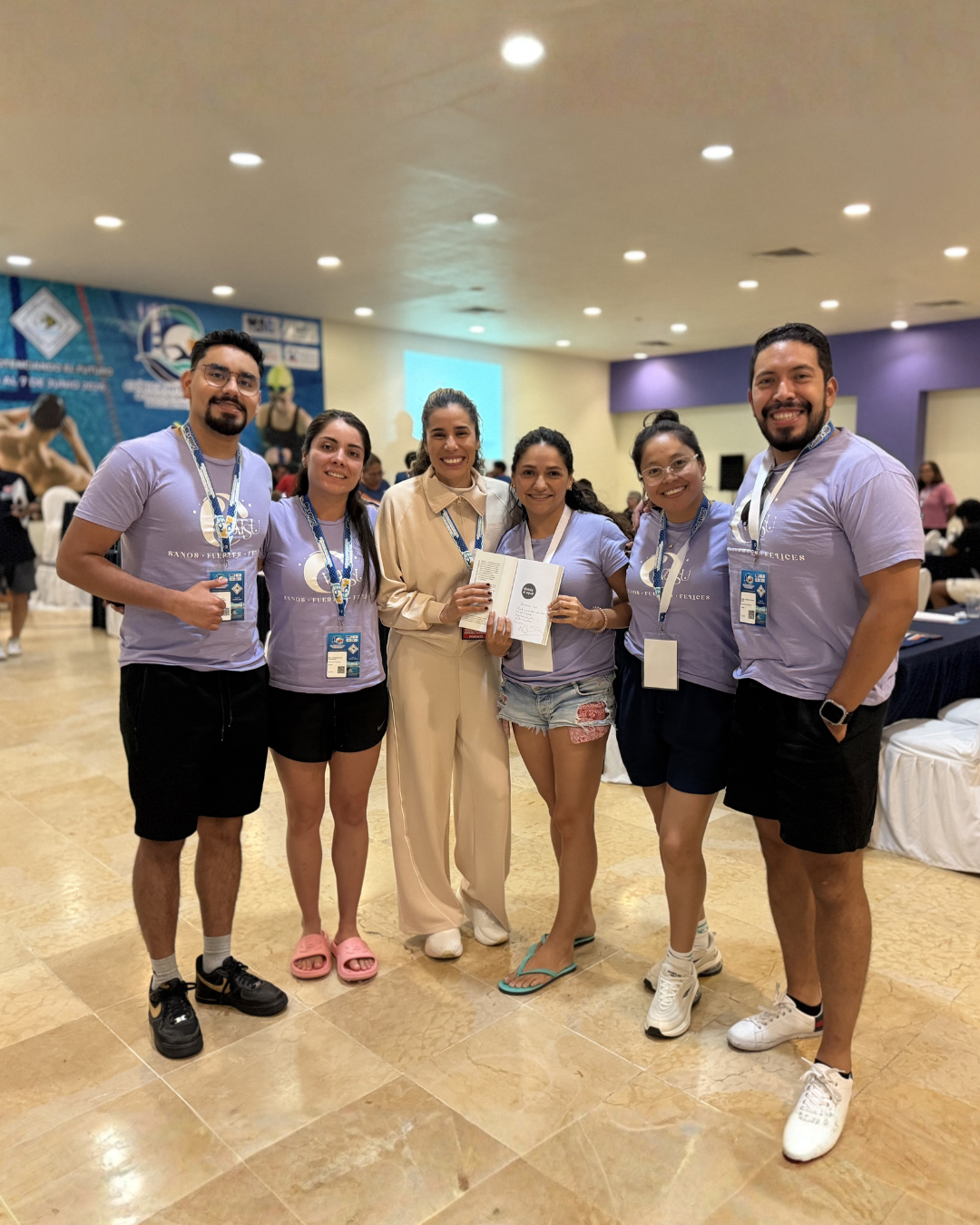 Cinco personas posando en el interior de un evento, sosteniendo un certificado y llevando cordones identificativos.