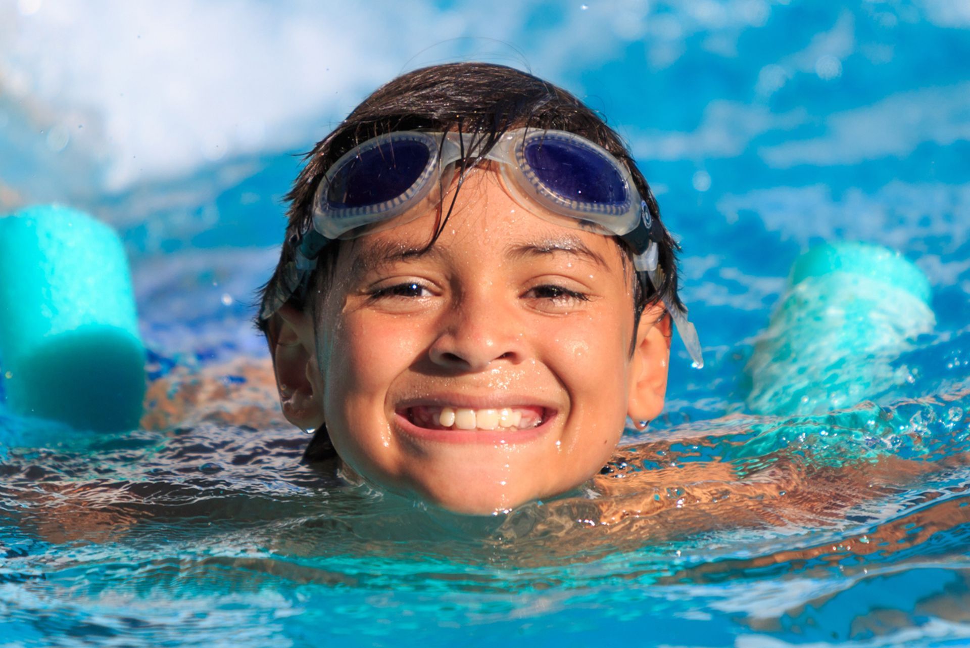 Nadador sonriente con gafas azules flotando en el agua azul brillante de una piscina.