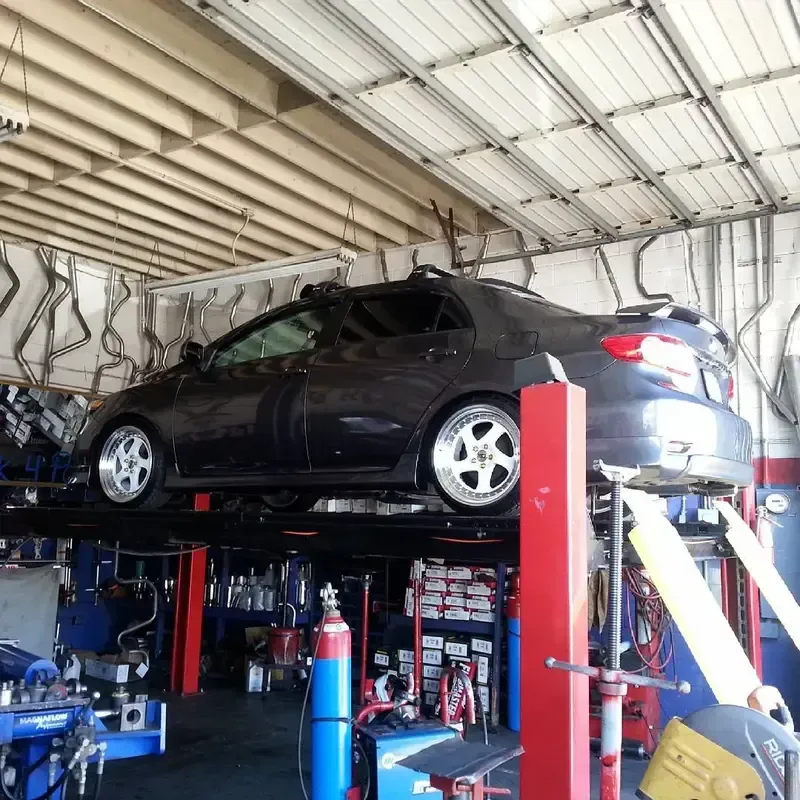A dark gray car on a hydraulic lift inside a garage; tools and equipment visible.
