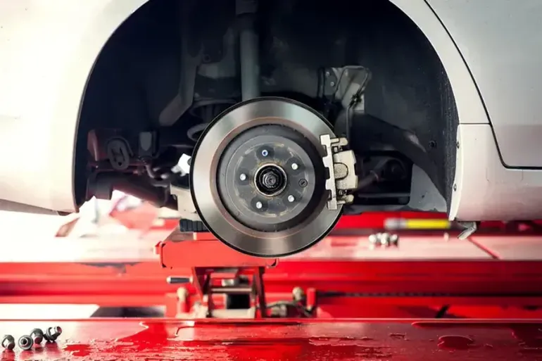Car brake rotor, caliper, and suspension components on a lift in a garage.