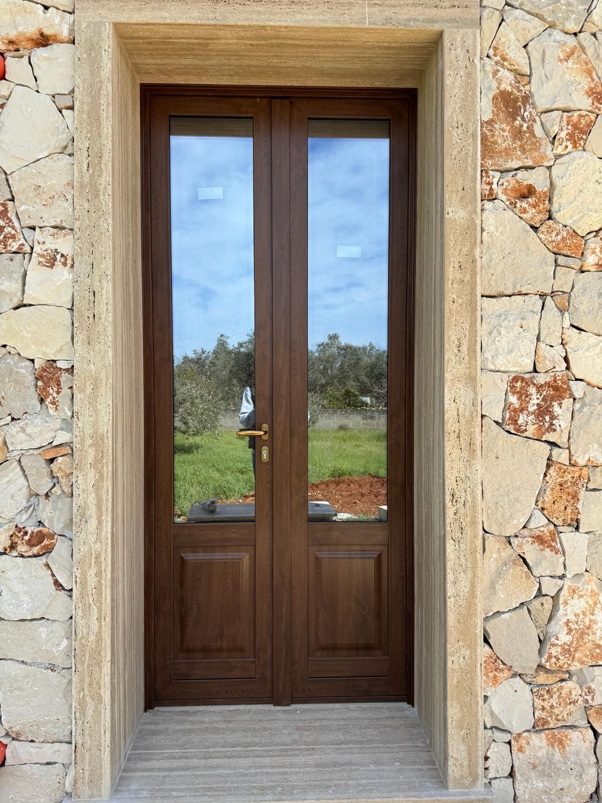 Doppie porte in legno marrone con vetri, incastonate nel muro di pietra.