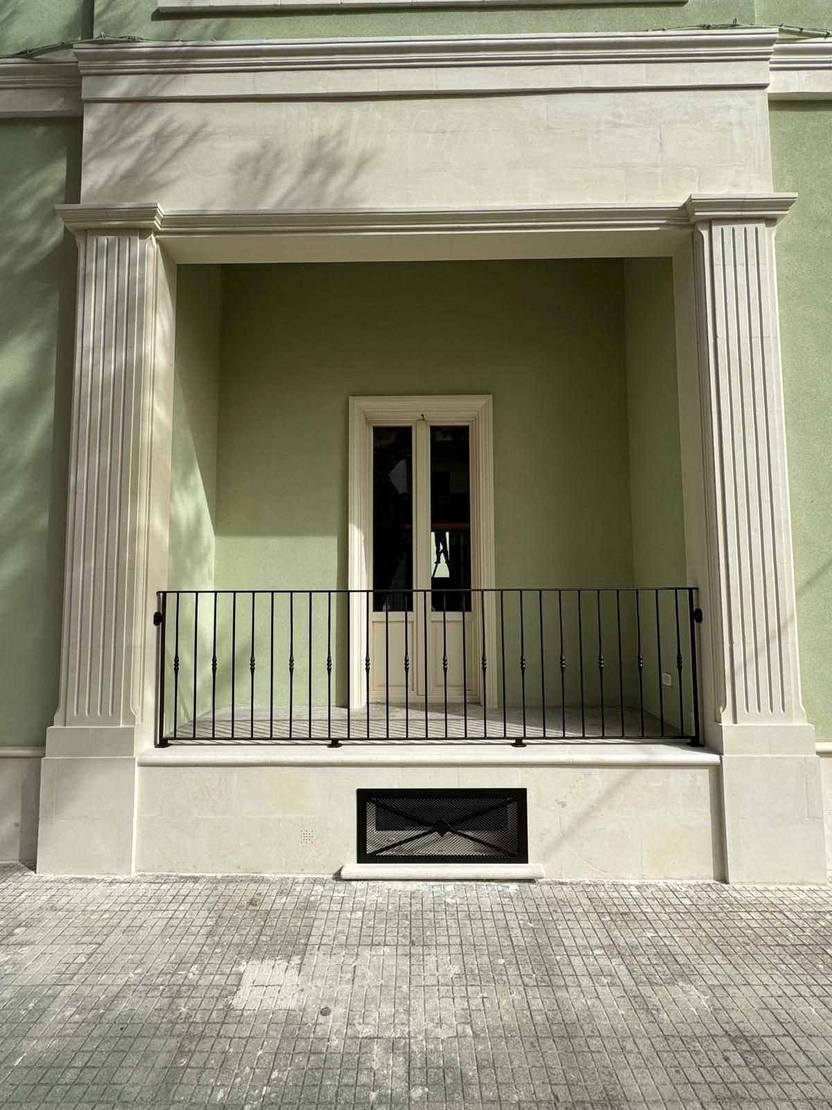 Un portale incorniciato da colonne, con una ringhiera nera e una finestra sottostante; l'edificio è verde chiaro.