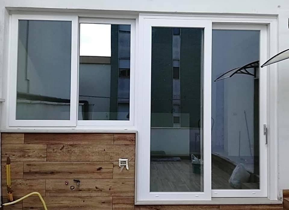 Porta scorrevole in vetro bianco e finestra, accanto a una parete rivestita in legno.