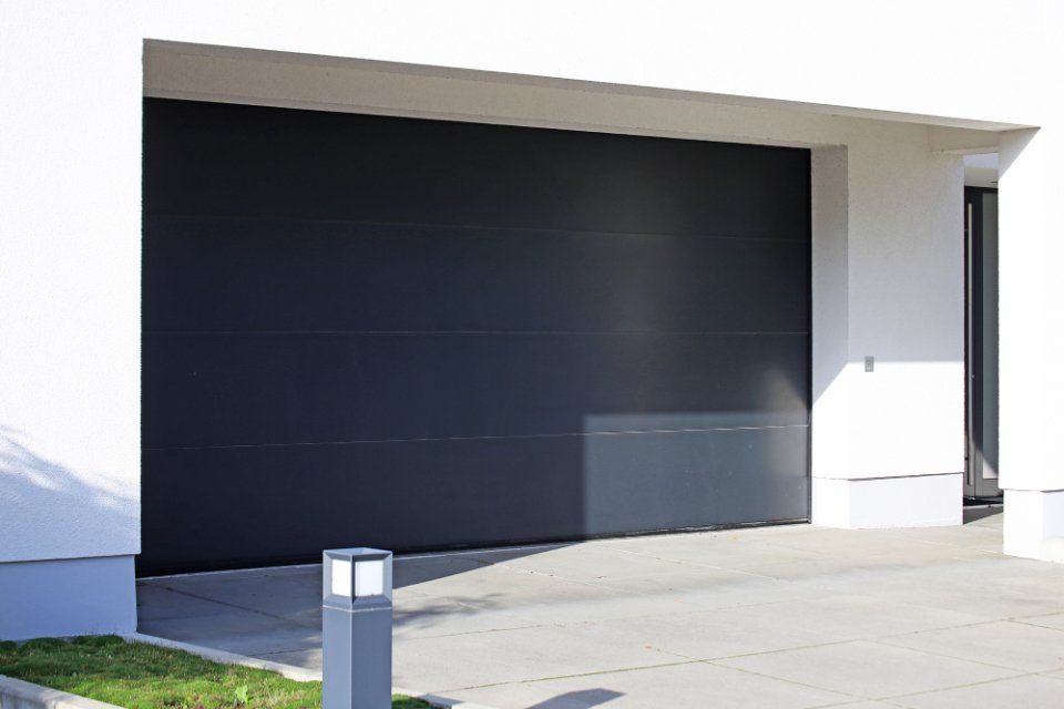 Porta da garage grigio scuro su un moderno edificio bianco con vialetto in cemento.