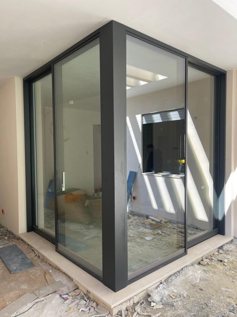 Porte scorrevoli angolari in vetro con telai scuri, che mettono in mostra uno spazio interno non rifinito.
