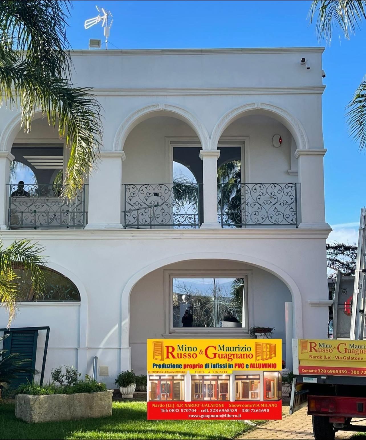 Edificio bianco a due piani con finestre ad arco. Un'insegna sulla facciata pubblicizza i servizi di vetreria. 