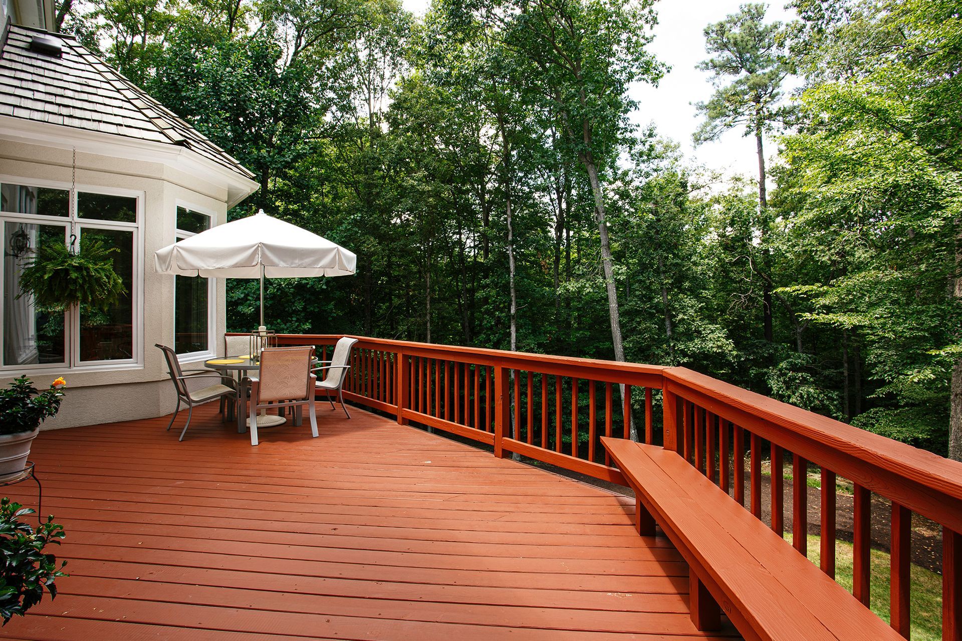 Wooden deck with seating and umbrella, overlooking a lush green forest.