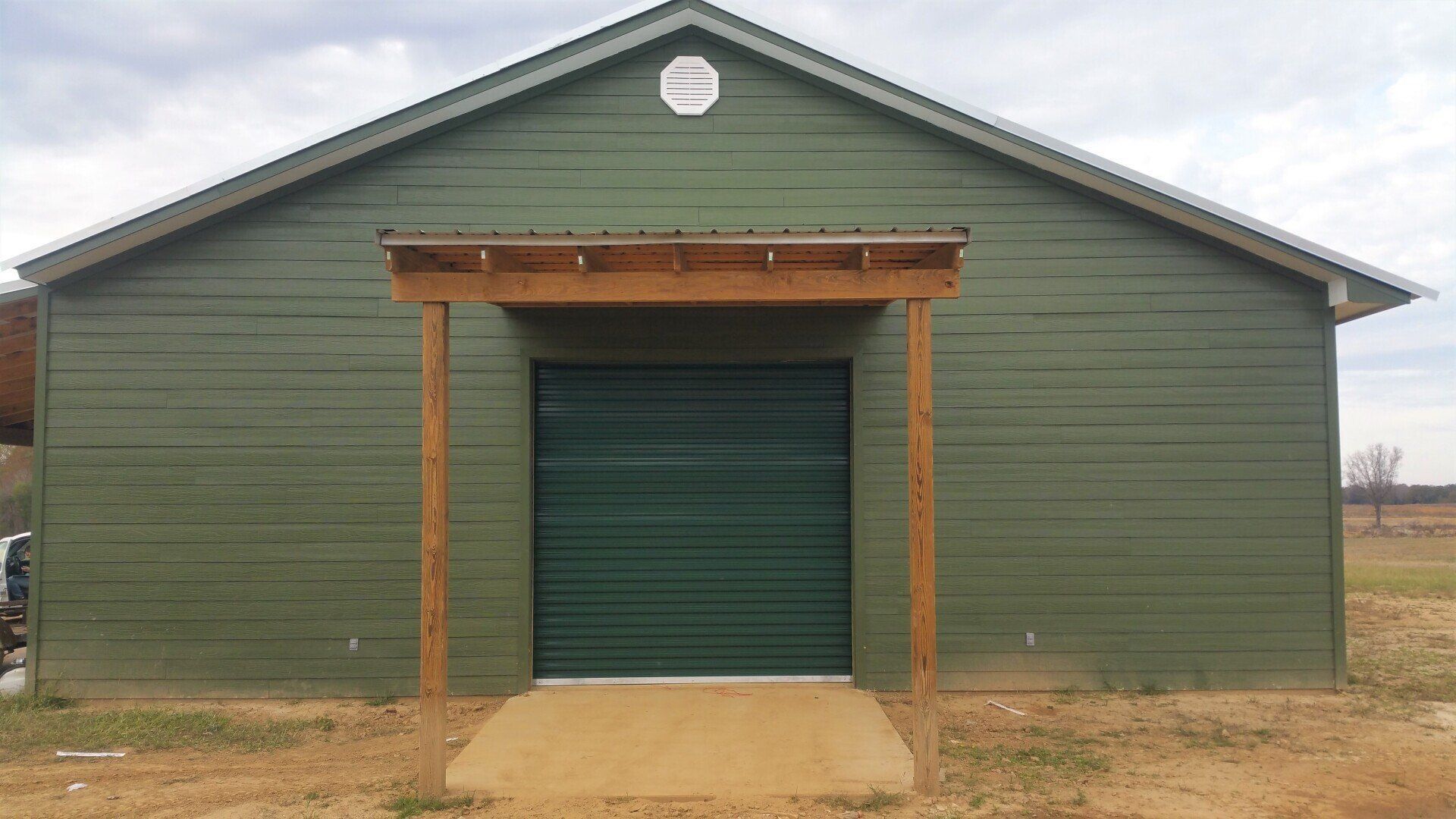 A green building with a green garage door is sitting in the middle of a field.