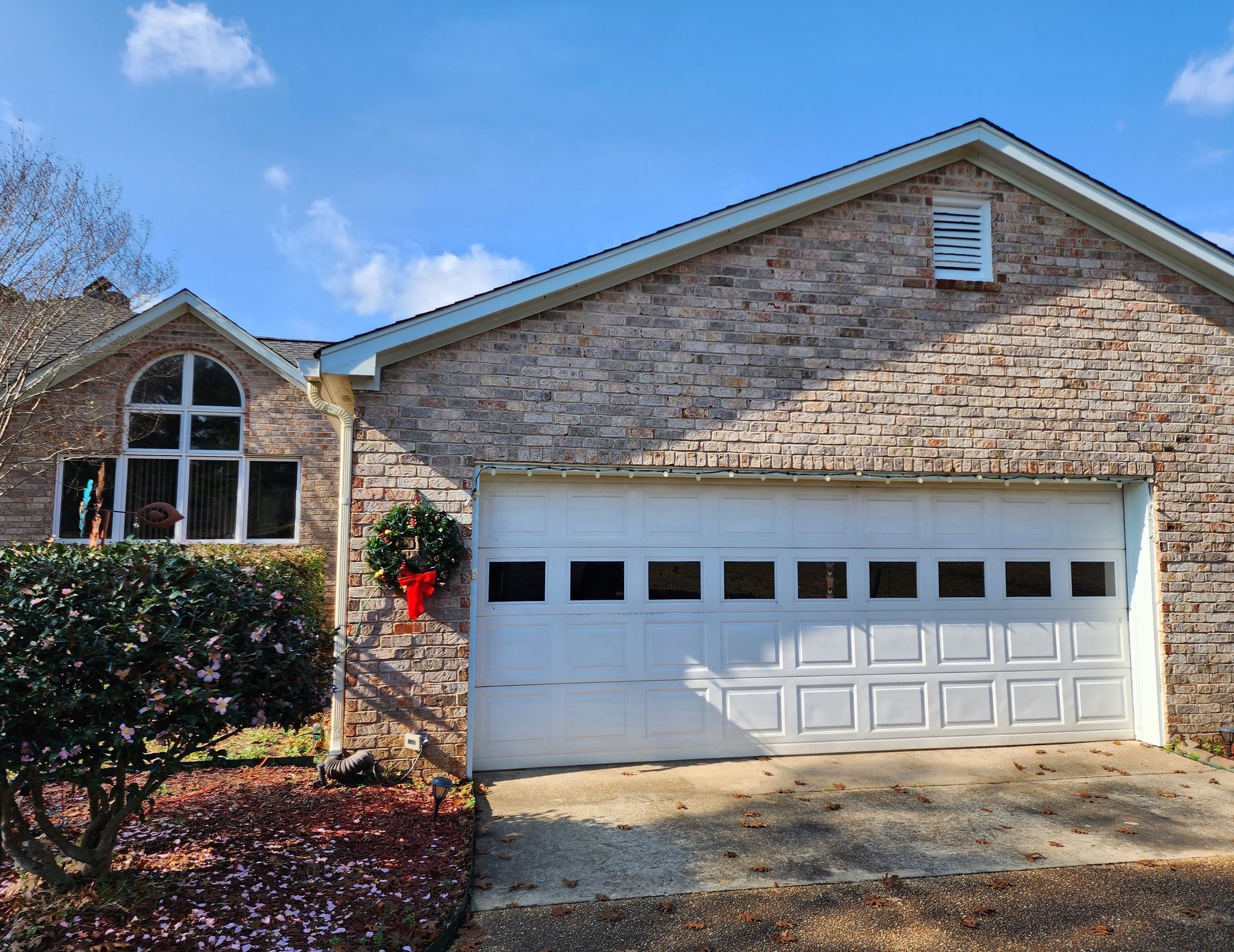Brick house with white garage door and arched window under a blue sky.