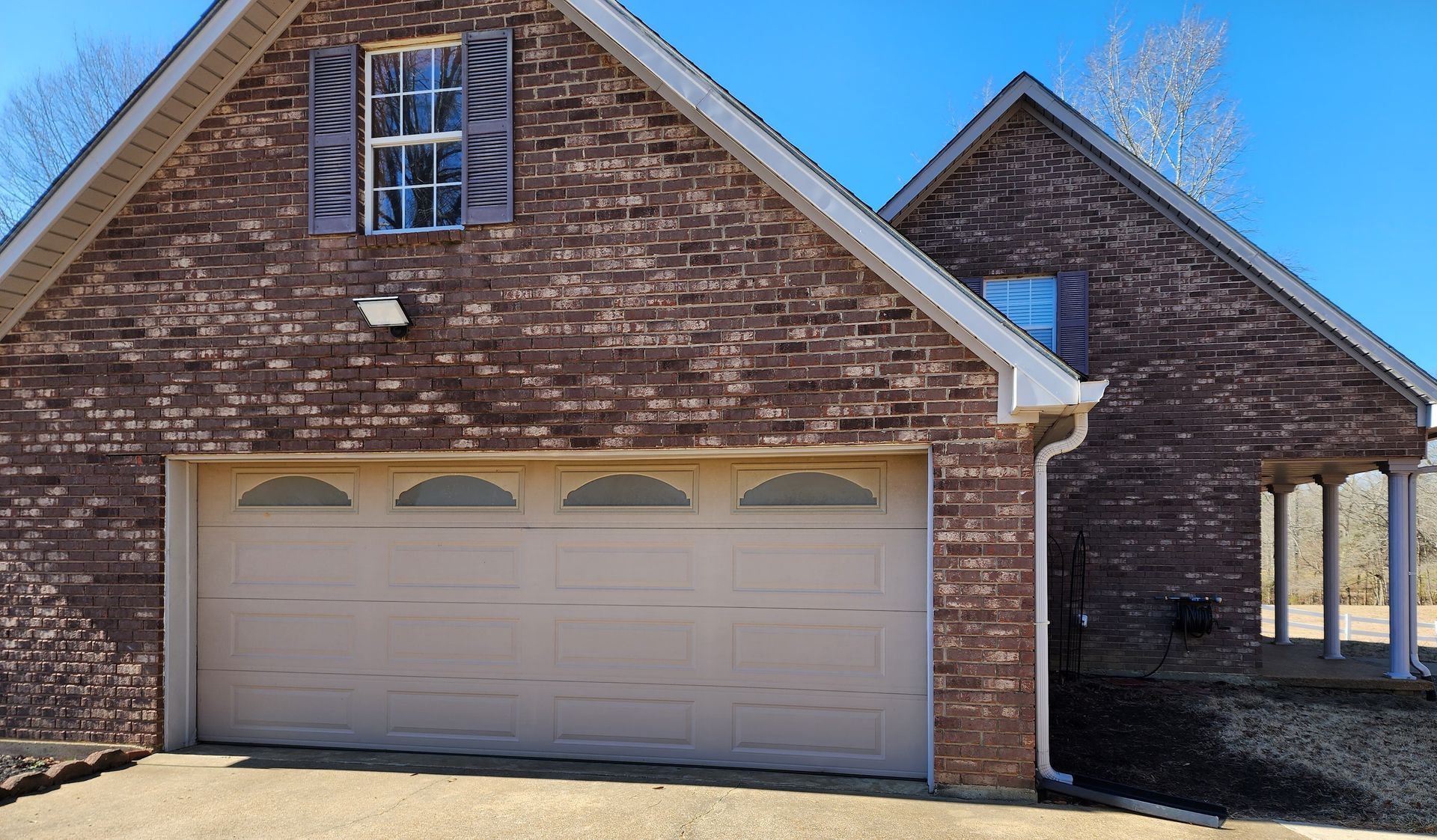 Brick house with beige garage door and shutters, clear sky.
