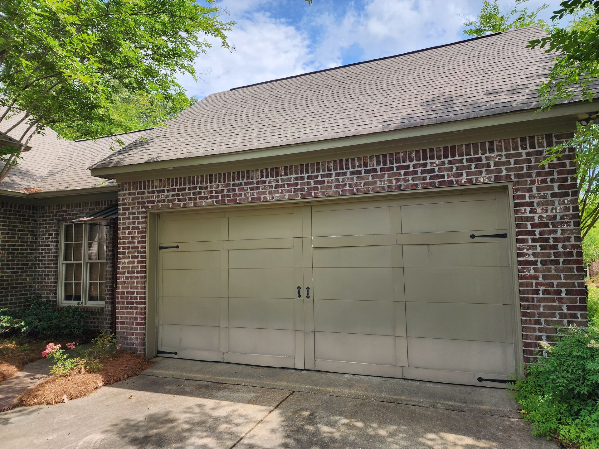 Garage with a brown brick exterior, olive-colored door, and shingle roof under a blue sky.