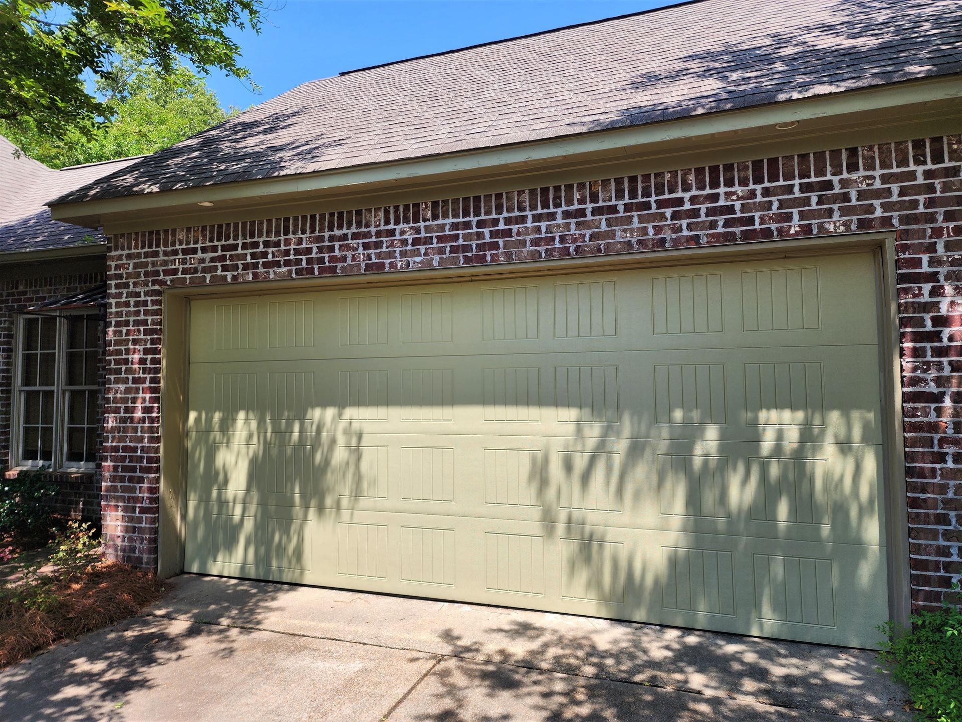 Garage door painted a light green color on a brick house.