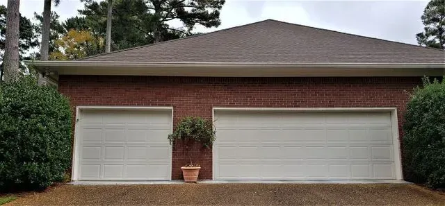 A brick garage with two white double doors, flanked by green shrubs.