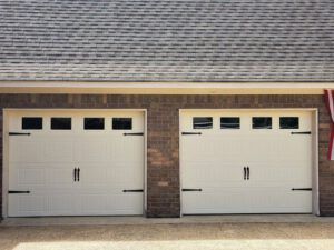 Two white garage doors on a brick building with an american flag hanging from the roof.